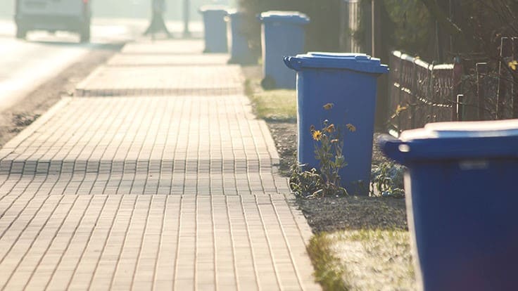 blue recycling bins lined up on brick sidewalk