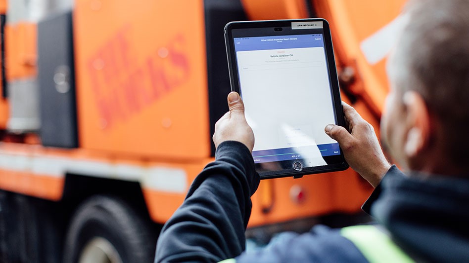 a man holding a tablet with a garbage truck in background