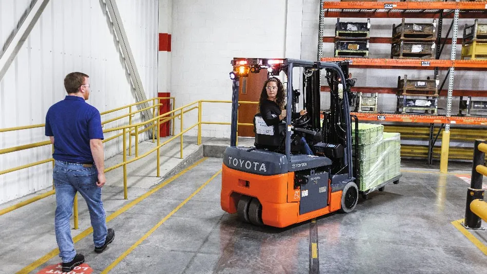 One person operates a forklift while another watches inside a facility