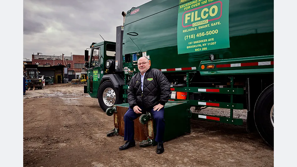 Domenic Monopoli sits in front of a green Filco Carting waste truck