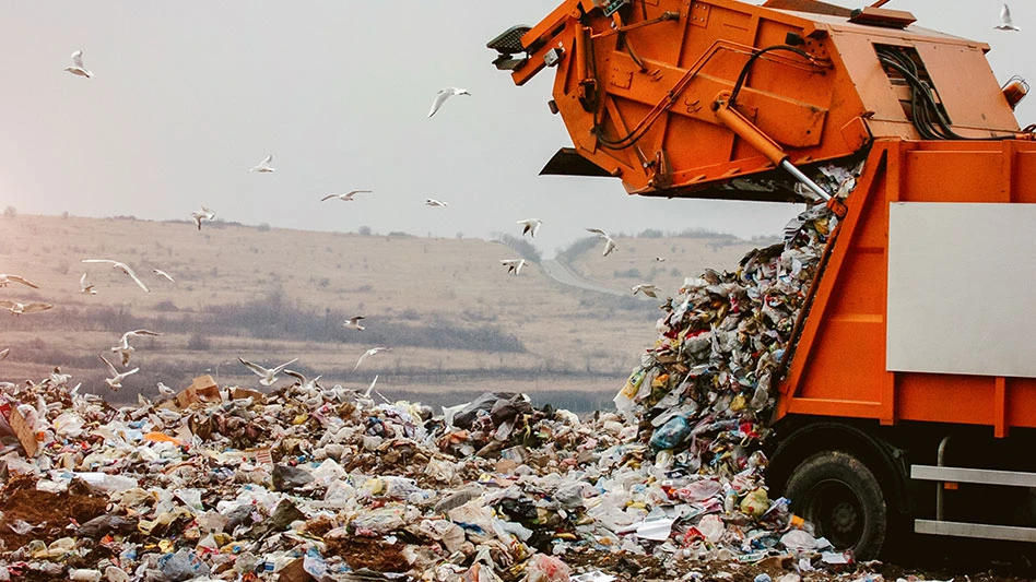 orange garbage truck dumps waste at landfill