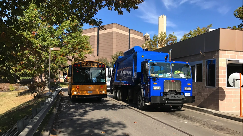 EV waste truck drives by school bus on residential street