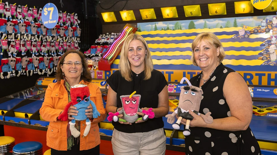 three women in front of carnival game holding prizes