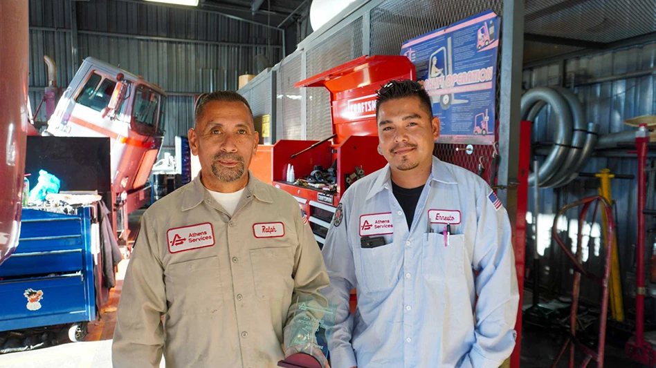 two men in athens uniforms smile in a workshop