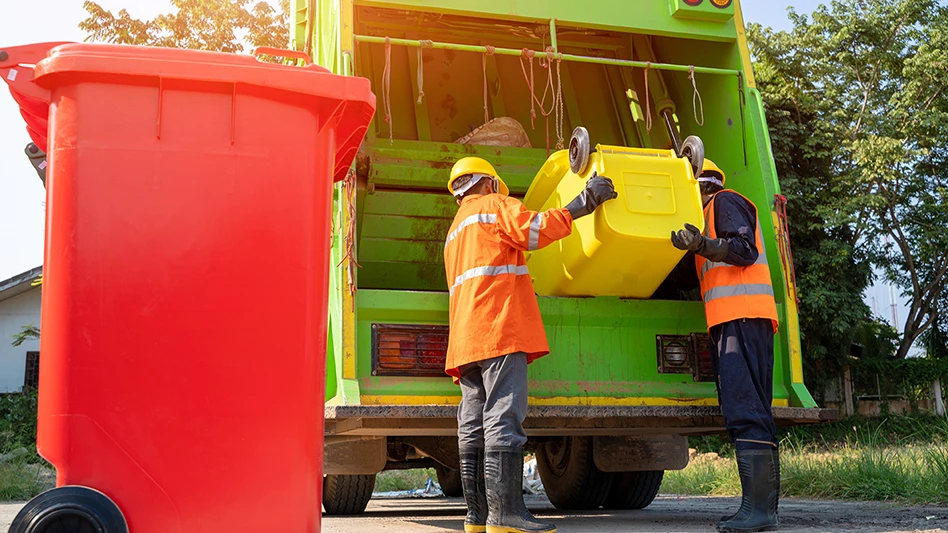 two men empty a garbage can into a truck with a red garbage can in the foreground