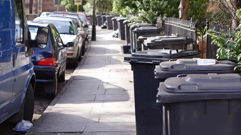 trash cans on the sidewalk parallel to cars parked on the street