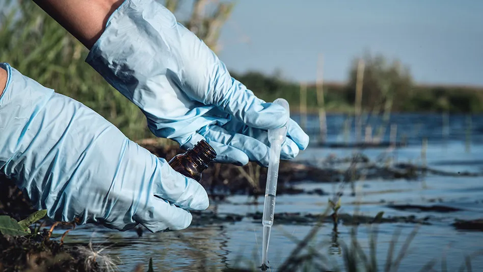 a person with light blue rubber gloves dips plastic pipette into water