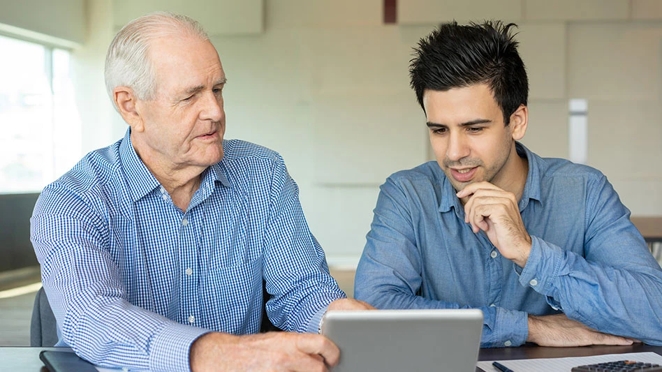 a grey haired balding man shows a young dark haired man something on a tablet