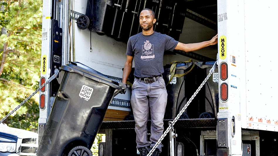 black man stands in back of white truck while holding onto organics disposal bin