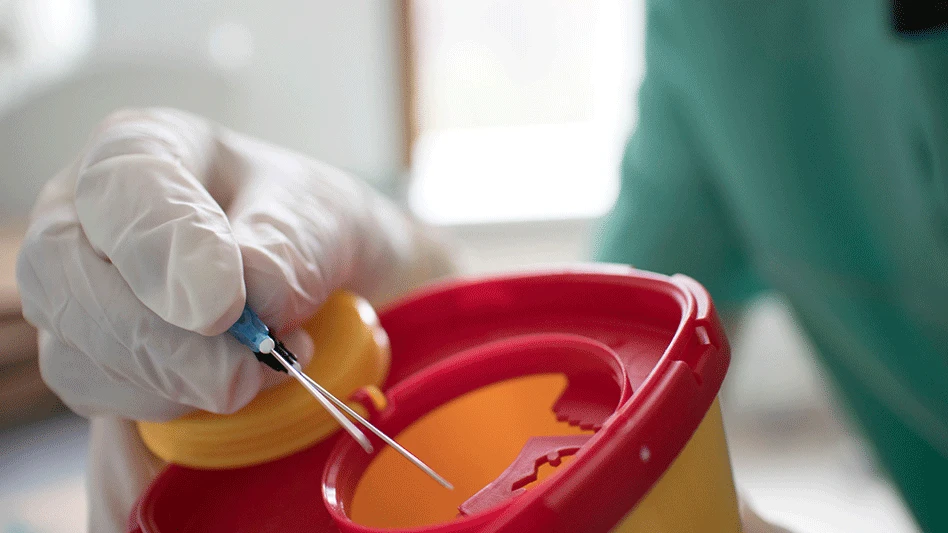 doctor with gloves on disposal of syringe in plastic container