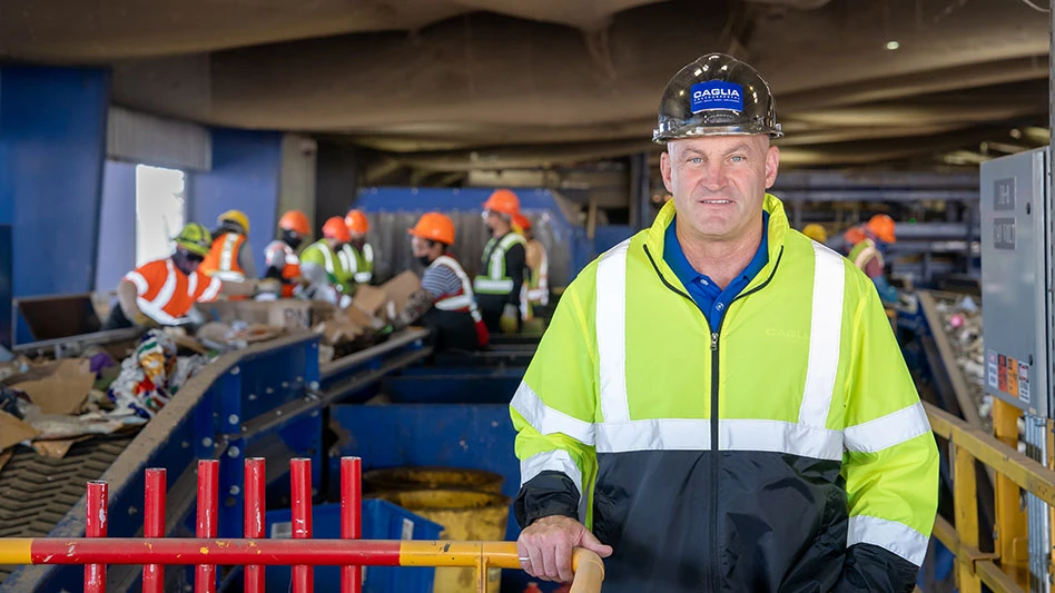 a man in a hard hat and reflective jacket stands in front of sorters working in a MRF