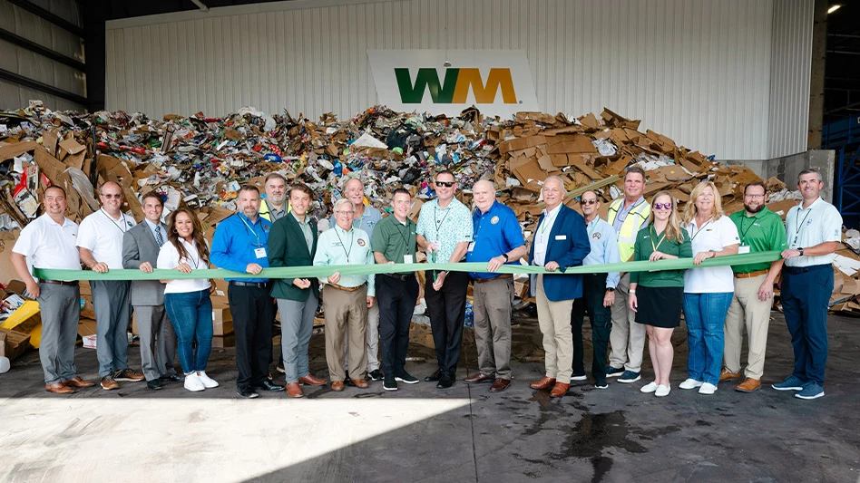 a group of people hold a ribbon on the tipping floor of the wm fort walton beach recycling facility