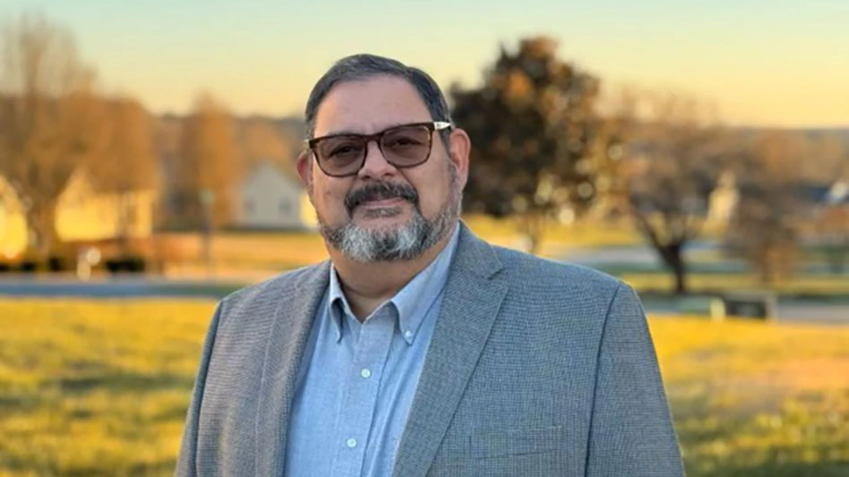a man with a gray and black beard wearing tinted glasses and a suit jacket smiles