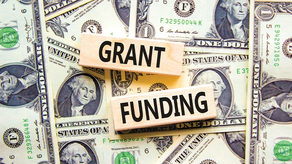 "Grant funding" written on wooden blocks, in front of a background of $1 bills.