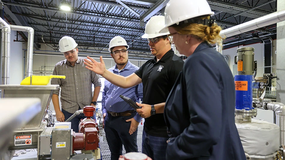 people in hard hads stand around a piece of equipment