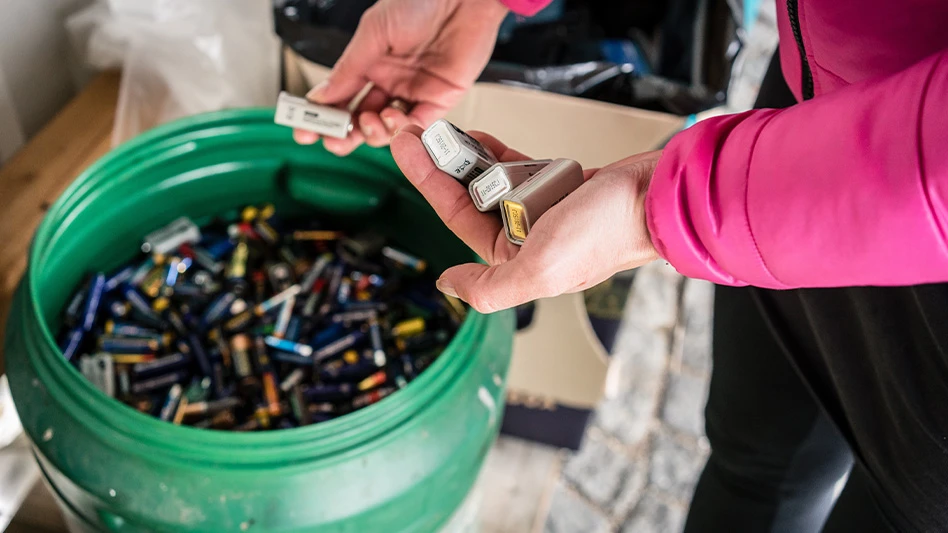 person in bright pink shirt (right) holding batteries and putting them in a green bucket full of batteries