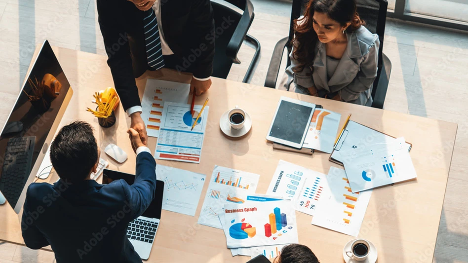 Adobe stock image of four people making a business deal at a table, showing two of them shaking hands.