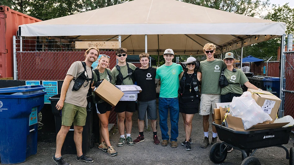 group of people standing under tent surrounded by cardboard and recycling/compost bins